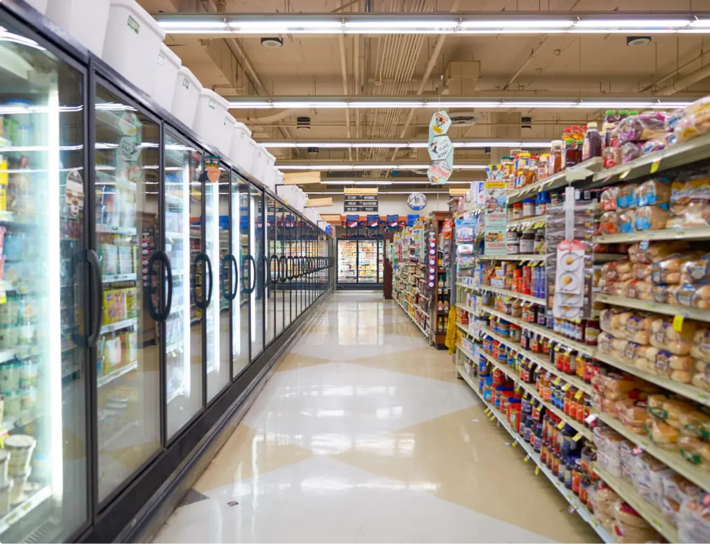 Vue d'un allée de supermarché, avec des réfrigérateurs sur la gauche et des étagères chargées de produits secs sur la droite.
